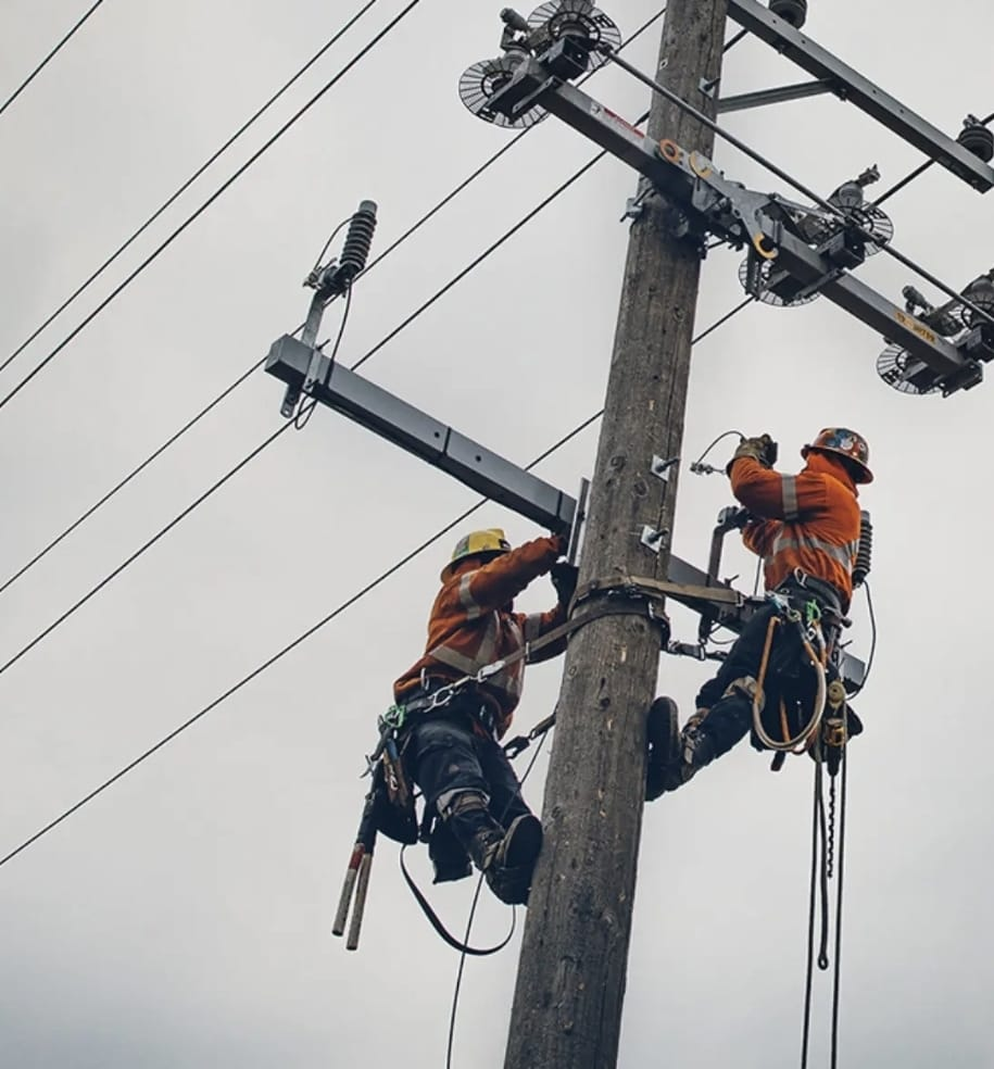 Two safety-equipped electrical workers installing hardware on a utility pole